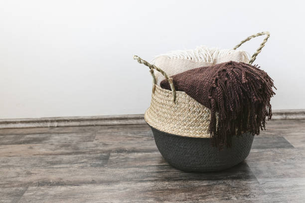 Trendy design handwoven seagrass belly basket with handles for storage laundry and toys with throws inside Handwoven seagrass belly or blanket basket with handles with beige and brown throws. Trendy natural multifunctional container for storage laundry, grocery, toy, plant in home. Side view, copy space blanket stock pictures, royalty-free photos & images