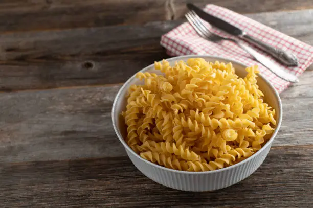 Italian pasta, fusilli in a rustic bowl on wooden table background from above with copy space