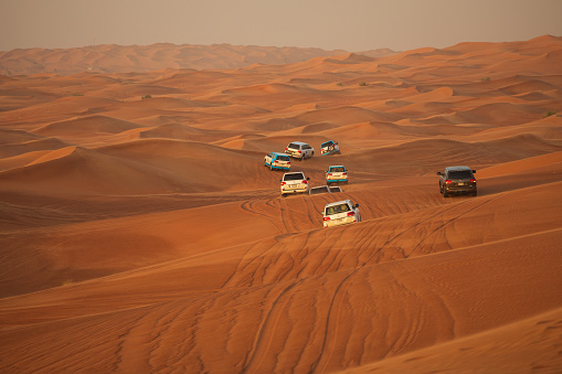 Off-road adventure with SUV driving in Arabian Desert at sunset, Off road vehicle bashing through sand dunes in Dubai desert, Traditional entertainment for tourists with car caravan
