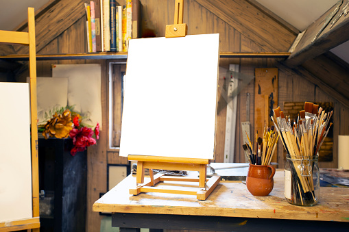 Artistic equipment in a artist studio: empty artist canvas on wooden easel and paint brushes Retro toned photo copy space space for text