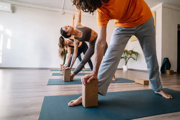 Barefoot man and women doing Triangle pose with block on mat during yoga session in spacious light studio