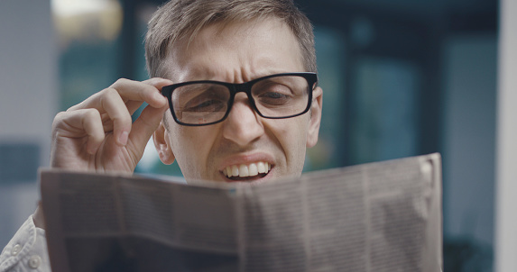 Man having a vision problem while reading a newspaper, he is adjusting his glasses