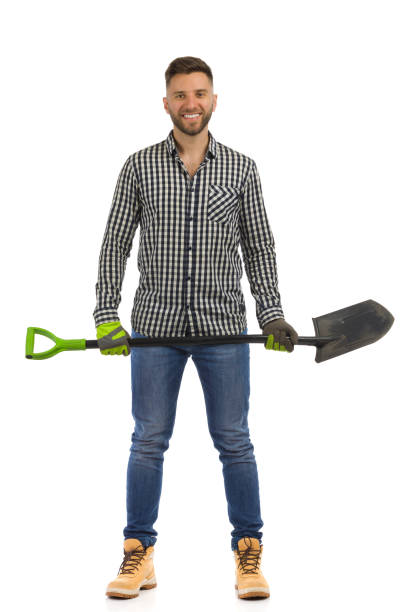 smiling toung man in lumberjack shirt is standing with spade. front view. studio shot. - toung imagens e fotografias de stock