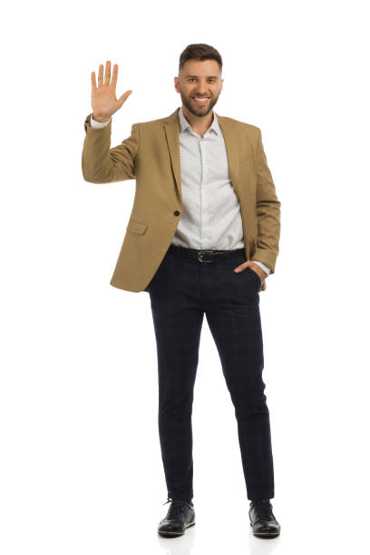 istock Elegant man in beige jacket is standing with hand raised. Front view. Full length isolated. 1363250521