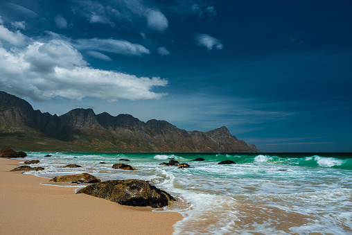 Sunshine on the beach with turquois waves and mountain range in Cape Town