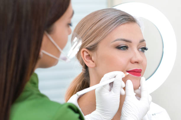 istock Young woman having permanent makeup on her lips at the beauticians salon. 1363257324