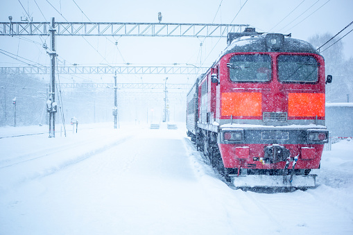Red locomotive at a snow-covered railway station in a blizzard and snowstorm.