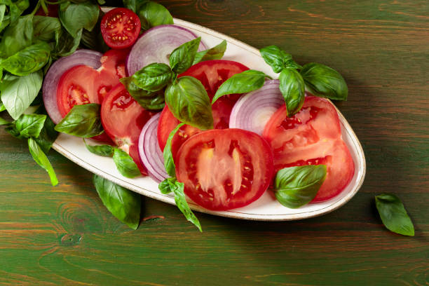 Salad with tomatoes, basil, and red onion on an old wooden table.