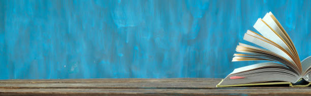 istock Open book, hardback book on wooden table on blue background. Back to school,education,reading.Panoramic free copy space 1363264746
