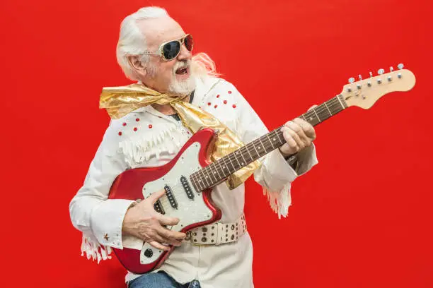 Senior guitarist playing his favorite rock'n'roll song - Old dressed up man who enjoys playing the guitar