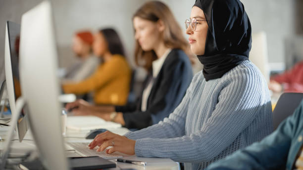 istock Curious Female Muslim Student Wearing a Hijab, Studying in Modern University with Diverse Multiethnic Classmates. College Scholars Work in College Room, Learning IT, Programming or Computer Science. 1363276337