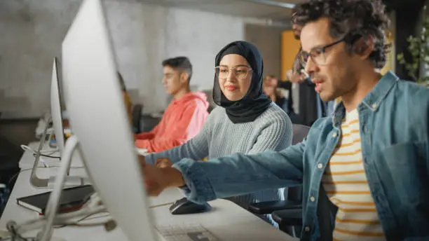 Photo of Female Muslim Student Wearing Hijab, Studying in Modern University with Diverse Multiethnic Classmates. She Asks Scholar a Question in College Room. Lecturer Shares Knowledge with Smart Scholars.