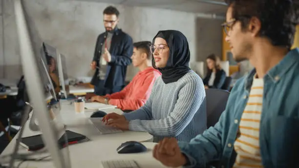 Photo of Female Muslim Student Wearing Hijab, Studying in Modern University with Diverse Multiethnic Classmates. She Asks Scholar a Question in College Room. Lecturer Shares Knowledge with Smart Scholars.