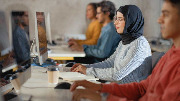 istock Curious Female Muslim Student Wearing a Hijab, Studying in Modern University with Diverse Multiethnic Classmates. College Scholars Work in College Room, Learning IT, Programming or Computer Science. 1363276443