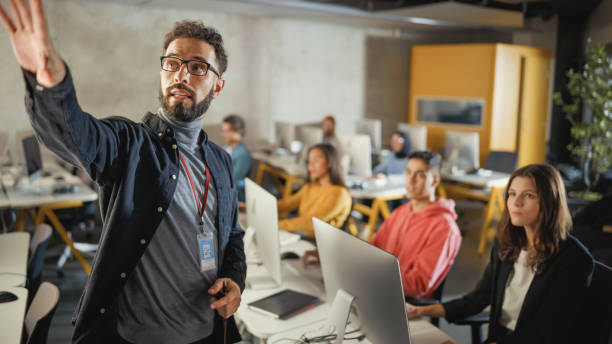 insegnante che tiene lezioni a diversi gruppi multietnici di studenti femminili e maschili nella stanza del college, imparando nuove abilità accademiche su un computer. docente condivide le conoscenze con giovani studiosi intelligenti. - teacher professor science university foto e immagini stock