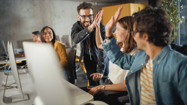 el profesor ayuda al becario con el proyecto, asesorando sobre su trabajo. maestra dando high five a un grupo multiétnico diverso de estudiantes femeninos y masculinos en la sala de la universidad, enseñando ingeniería de software. - teacher professor science university fotografías e imágenes de stock