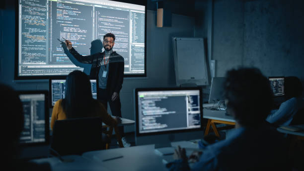 un enseignant donne une conférence en informatique à un groupe multiethnique diversifié d’étudiants féminins et masculins dans une salle sombre du collège. projection d’un diaporama avec du code de programmation. expliquer les technologies de l� - stage photos et images de collection