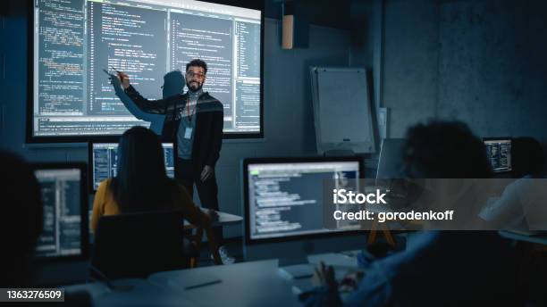 Teacher Giving Computer Science Lecture To Diverse Multiethnic Group Of Female And Male Students In Dark College Room Projecting Slideshow With Programming Code Explaining Information Technology Stock Photo - Download Image Now