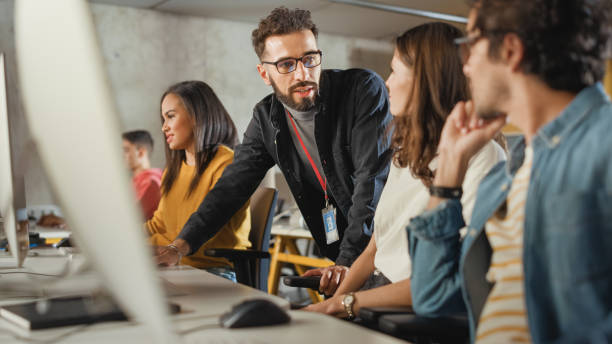 istock Lecturer Helps Scholar with Project, Advising on Their Work. Teacher Giving Lesson to Diverse Multiethnic Group of Female and Male Students in College, Teaching Computer Science and Writing Code. 1363276542