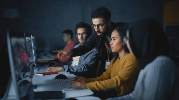 istock Lecturer Helps Scholar with Project, Advising on Their Work. Teacher Giving Lesson to Diverse Multiethnic Group of Female and Male Students in College Room, Teaching New Academic Skills on a Computer. 1363276559