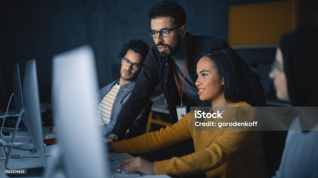 Lecturer Helps Scholar with Project, Advising on Their Work. Teacher Giving Lesson to Diverse Multiethnic Group of Female and Male Students in College Room, Teaching New Academic Skills on a Computer. Computer Programmer Stock Photo