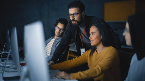 palestrante ajuda estudioso com projeto, aconselhando sobre seu trabalho. professor dando aula para diversos grupos multiétnicos de estudantes femininos e masculinos na sala da faculdade, ensinando novas habilidades acadêmicas em um computador. - computer programmer - fotografias e filmes do acervo