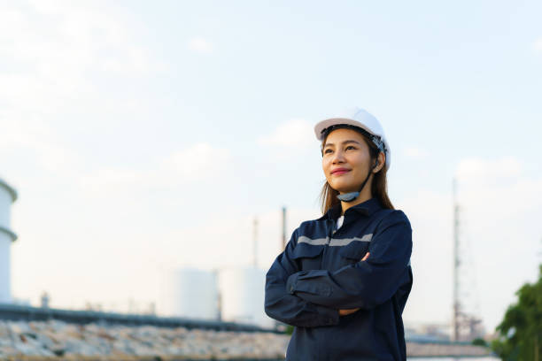 donna asiatica ingegnere braccio incrociato e sorriso con fiducioso guardando al futuro con la fabbrica di impianti di raffineria di petrolio sullo sfondo. - working platform foto e immagini stock