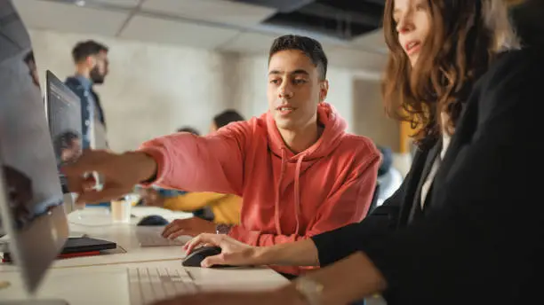 Photo of Diverse Multiethnic Group of Female and Male Students Sitting in College Room, Collaborating on School Projects on a Computer. Young Scholars Study, Talk, Apply Academic Skills and Knowledge in Class.