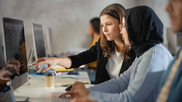 gruppo multietnico diversificato di studenti di sesso femminile e maschile seduti nella stanza del college, che collaborano a progetti scolastici su un computer. i giovani studiosi studiano, parlano, applicano le competenze accademiche e le conoscenze in c - velo foto e immagini stock