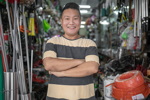 Asian Chinese man owner smiling looking at camera in front of hardware store.as