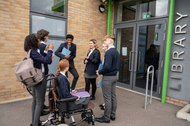 Mid-teen classmates gathered outside school library Full length view of diverse student group in uniforms standing outside education building talking and laughing. teenagers only teenager multi ethnic group student stock pictures, royalty-free photos & images