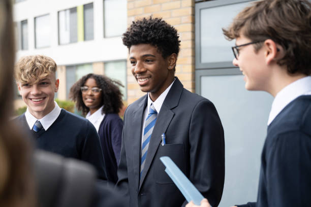 Cheerful students in mid-teens interacting between classes Waist-up view of diverse group wearing uniforms and talking as they stand outside secondary school building. teenagers only teenager multi ethnic group student stock pictures, royalty-free photos & images