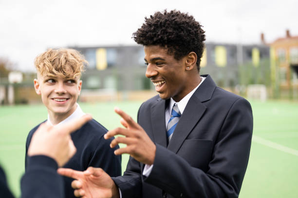 Candid outdoor portrait of playful schoolboys on campus Close-up of teenage students in uniforms standing outdoors on sports field talking, laughing, and gesturing. happy young teens stock pictures, royalty-free photos & images