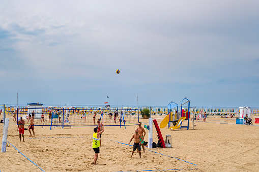Young adults playing beach volleyball on the beach of Bibione, one of the main destinations of summer tourism on the Adriatic riviera of Veneto.