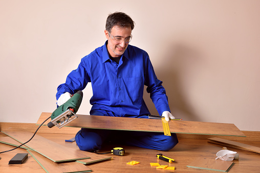 Professional parquet assembler with cutting machine ready to cut slat for mounting parquet in the home. Horizontal composition.