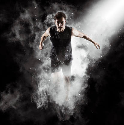 Sporty young man running on black smoke background