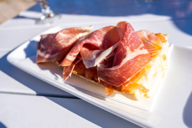 Detail of a slice of Serrano ham toast on a white table on the terrace of a cafeteria. stock photo