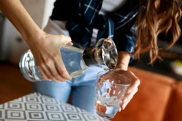 Woman pouring some fresh water into a glass from carafe