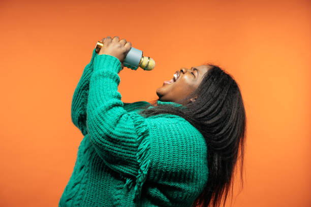 imagen de una hermosa mujer posando con ropa casual sobre un fondo de color. - singer singing women microphone fotografías e imágenes de stock