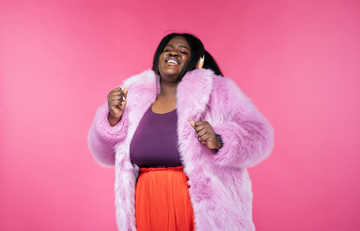 Image of a beautiful woman posing in a furry coat on a pink background