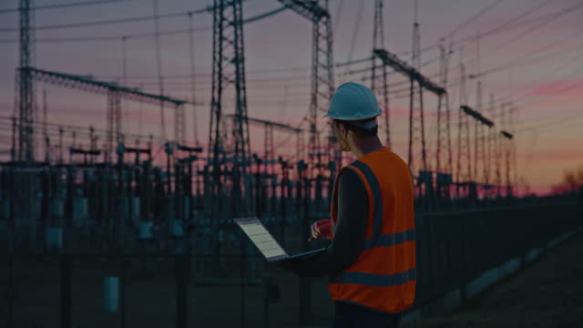 Confident male engineer using a laptop in front of electric power station