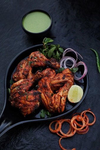 Tandoori chicken with onion and chutney on black background. Food photography and food styling.