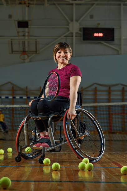 Disabled young woman on wheelchair playing tennis on tennis court stock photo