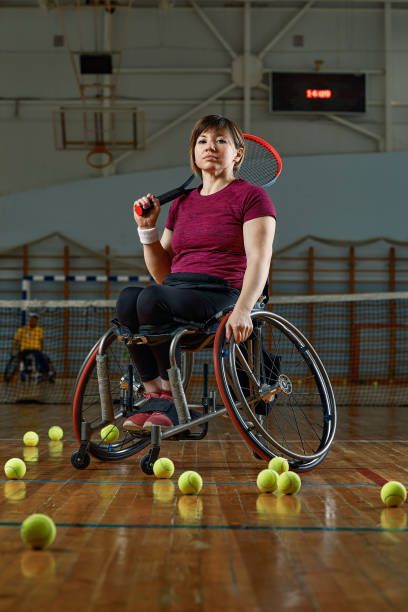 mujer joven discapacitada en silla de ruedas jugando al tenis en la cancha de tenis - wheelchair tennis physical impairment athlete fotografías e imágenes de stock