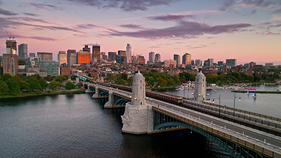 Aerial shot of Boston, Massachusetts at sunset, looking across the Charles River towards the downtown skyline as a red line train crosses by on the Longfellow Bridge. \n\nAuthorization was obtained from the FAA for this operation in restricted airspace.