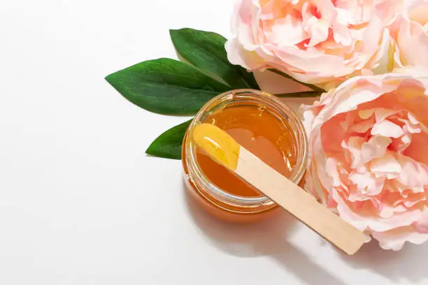 Photo of Liquid sugar paste for hair removal in a bowl with peony flower on white background.