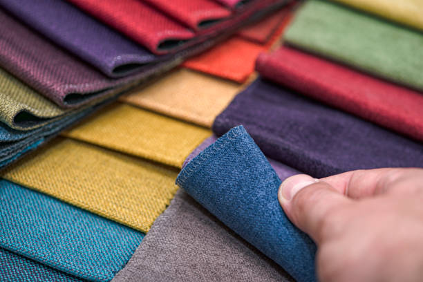 istock Samples of textiles for upholstery in different colors and thicknesses. Closeup details of multicolor fabric texture samples. A man takes a sample of fabric and checks its quality by touch 1363328071