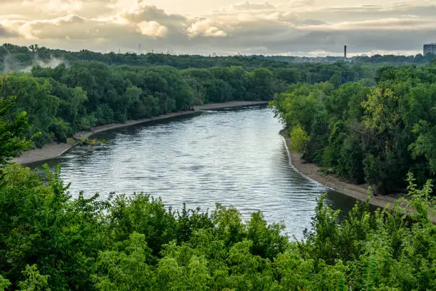 Wide angle view of the Mississippi River shore, outside of Minneapolis. Minnesota, Along the river shore are power pylons and electrical wires that follow the river.  On both sides of the river is dense vegetation and in the sky above are clouds from an impending storm,

Taken in Minneapolis. Minnesota, USA