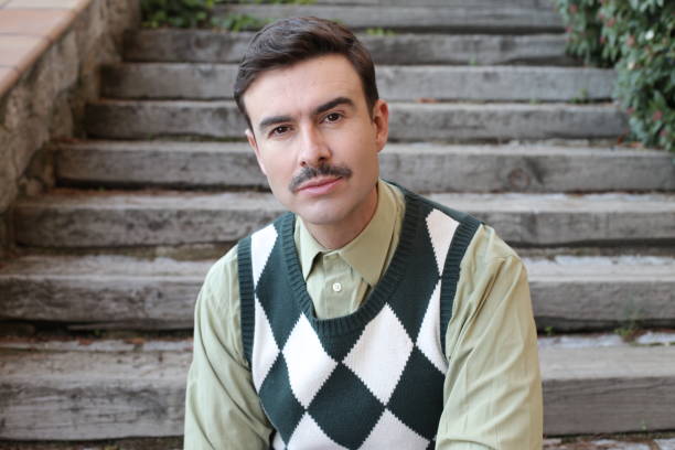 Man with a mustache wearing sleeveless rhombus sweater.
