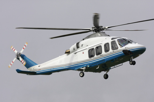 Blue and white corporate helicopter with landing gear down.
